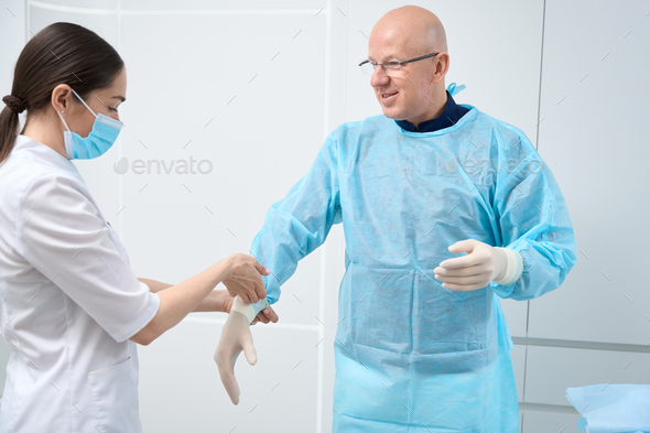 Professional female nurse assisting doctor with dressing in sterile equipment