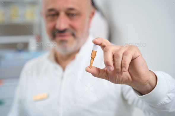 Elderly doctor holds an ampoule with medicine in his hand