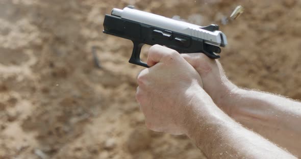 Slow motion close up shot of a man shooting a hand gun while moving backwards