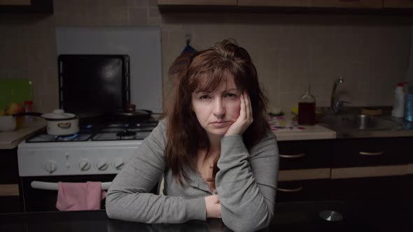 Boring Woman Sitting in the Kitchen in the Evening and Looking at the Camera