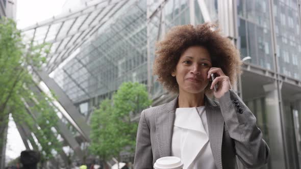 Afro American businesswoman in city using smart phone with takeaway coffee