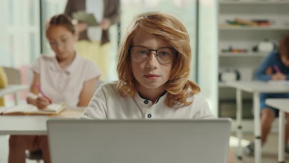Portrait of the Redhead Boy Sitting on the Desk with Laptop in a Class During Computer Science alt