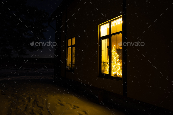 Cozy festive window of the house outside with the warm light of fairy lights garlands inside