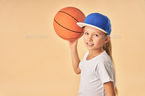Cheerful cute girl in cap plying basketball - Stock Photo - Images