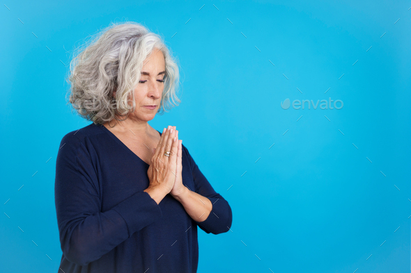 Mature woman praying with folded hands and closed eyes