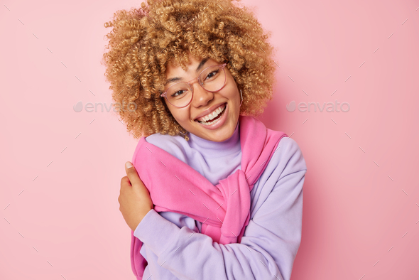 Happy lovely woman with curly bushy hair embraces herself hugs own body expresses self love and