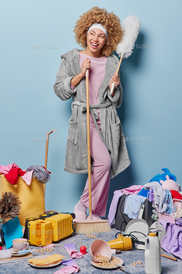 Positive housewife with curly hair does domestic work at home house cleanup cleans messy room tidies