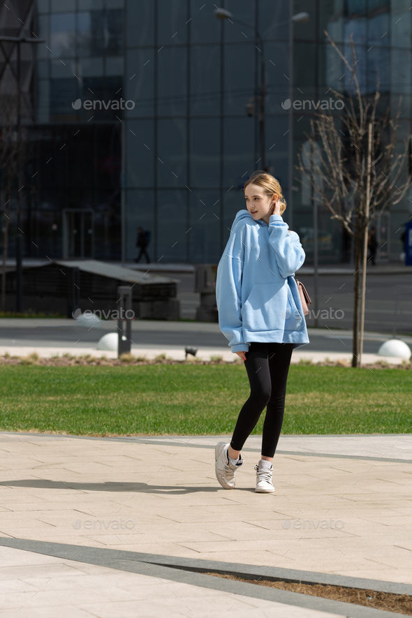 A teenage girl in a hoodie and leggings walks in the city Stock Photo by  natalya_ugr