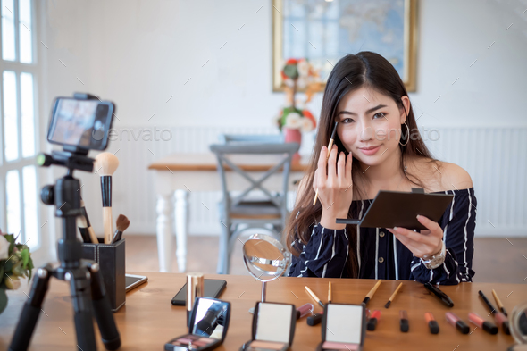 Young asian woman blogger with makeup cosmetics recording video clip online by smartphone at home. T