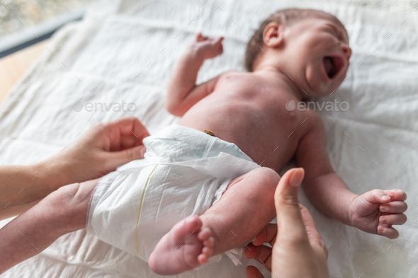Newborn baby screaming while mother puts a diaper on the changing table - Stock Photo - Images