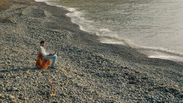 Slow Motion Young Man with a Beard and Mustache Works on a Laptop While Sitting on a Deserted alt
