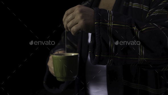 Man in a Bathrobe with a Cup of tea. Stock. A man makes tea on a black background. Bad mood concept