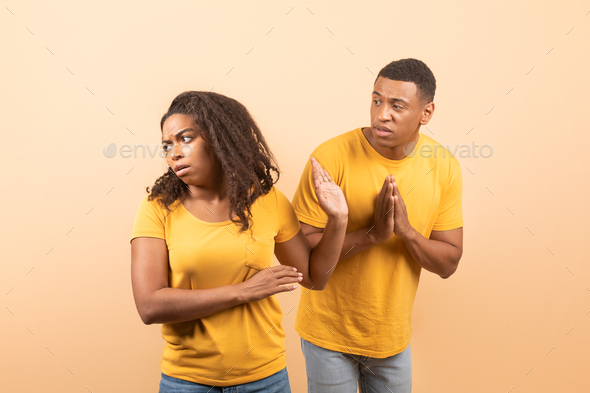 Black husband trying to talk and reconcile with offended wife, standing over yellow studio