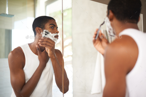 Getting rid of stubborn stubble. A young man shaving in the mirror.