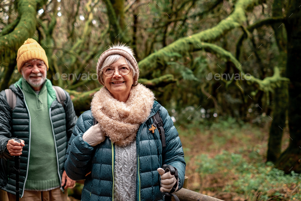 Old senior couple enjoying nature outdoors in a mountain forest with moss covered trunks