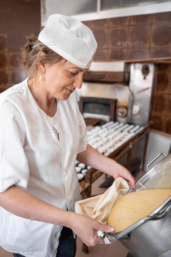 Baker woman filling a pastry bag with a dough in order to make cupcakes
