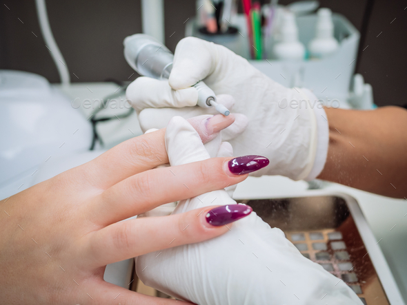 Professional esthetician using an electric nail file drill to remove acrylic gel from nails