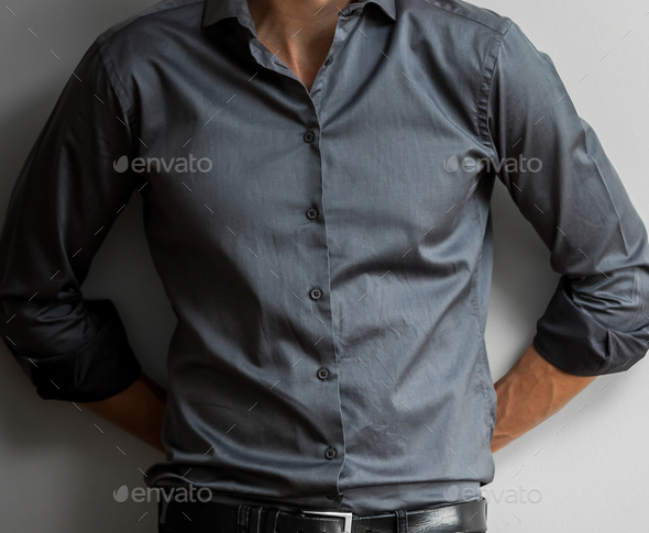 Mid-section of a sexy elegant man in a gray shirt with folded sleeves leaning against a wall