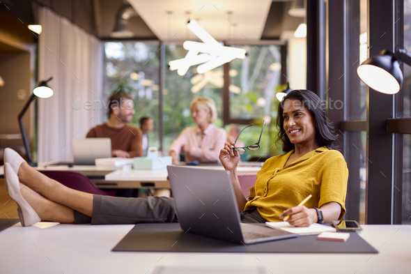 Mature Businesswoman With Feet On Desk Working On Laptop In Office Stock  Photo by monkeybusiness