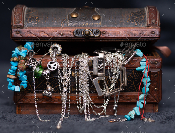Frontal shot of a brown jewelry box full of jewels isolated on the dark gray surface