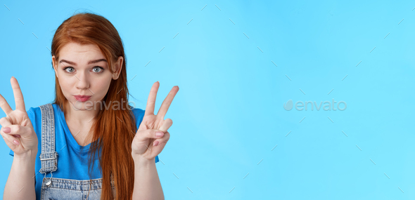 Playful cute silly redhead girlfriend making funny face, show peace victory signs, hold breath