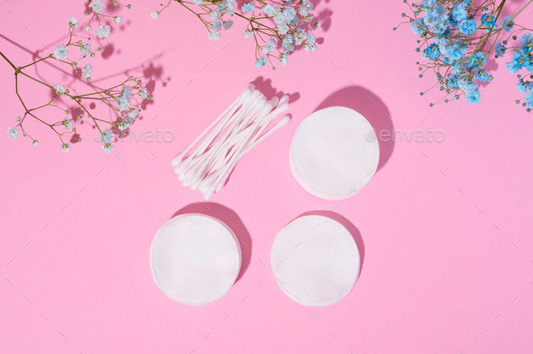 Round cotton cosmetic pads and cotton buds on a pink background