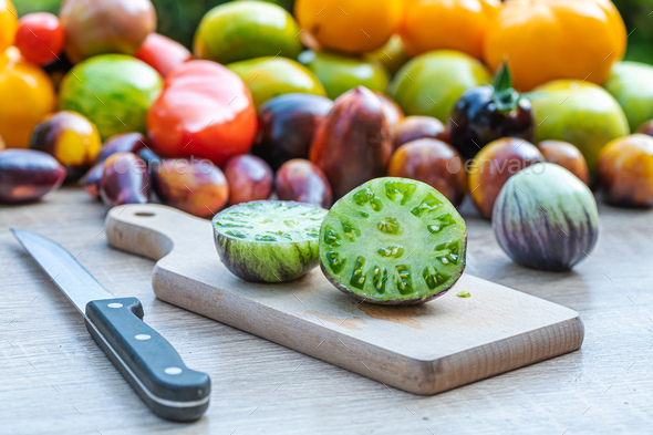 table with a cutting board with sliced tomatoes with different colored tomatoes in the background - Stock Photo - Images