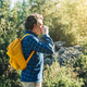 Adult male tourist with yellow backpack walking in forest. Young guy in casual clothes looking at - PhotoDune Item for Sale