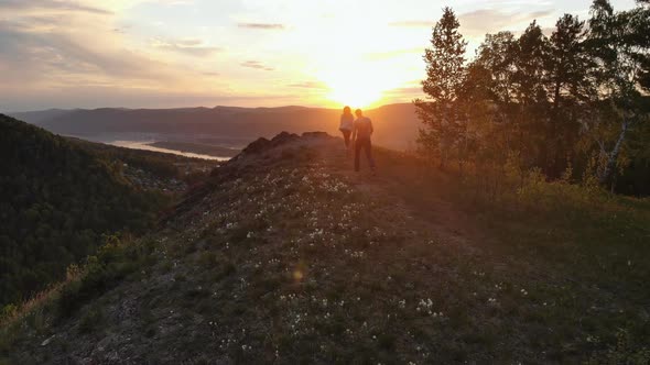 Aerial Shot of a Young Couple Running To the Top of a Mountain at Sunset