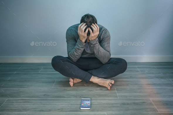 Man with problems sitting on the floor behind of his mobile - Stock Photo - Images