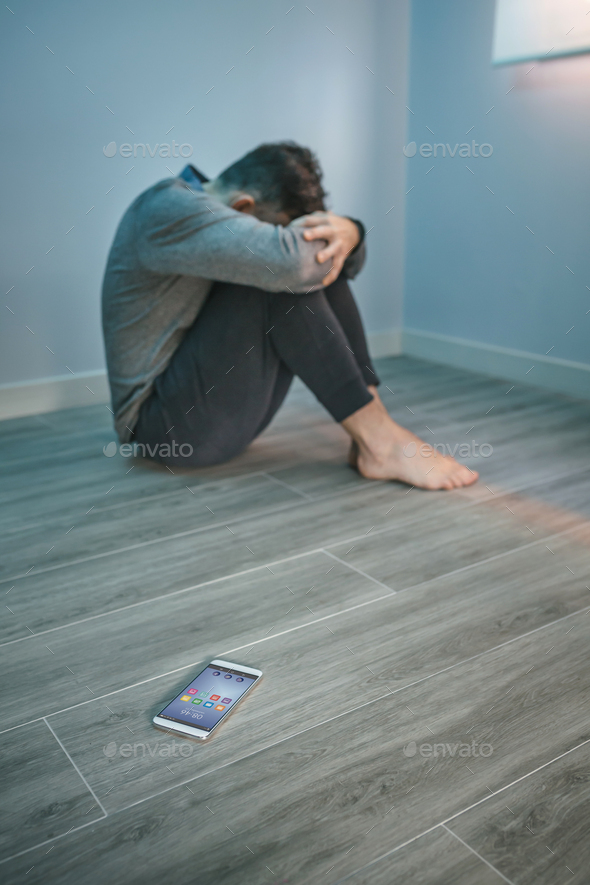 Man with problems sitting on the floor with mobile on the floor - Stock Photo - Images