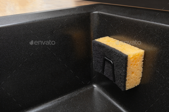 Organizer holder for a kitchen sponge in a black granite sink. Storage and organization of space