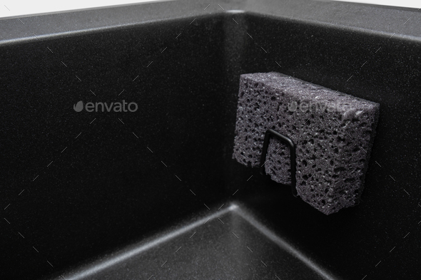 Organizer holder for a kitchen sponge in a black granite sink. Storage and organization of space