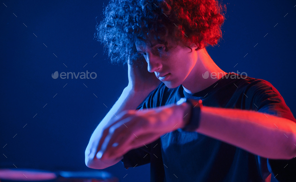 DJ is in the club. Young man with curly hair is indoors illuminated by neon lighting