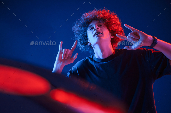 Dj is playing music from vinyl. Young man with curly hair is indoors illuminated by neon lighting