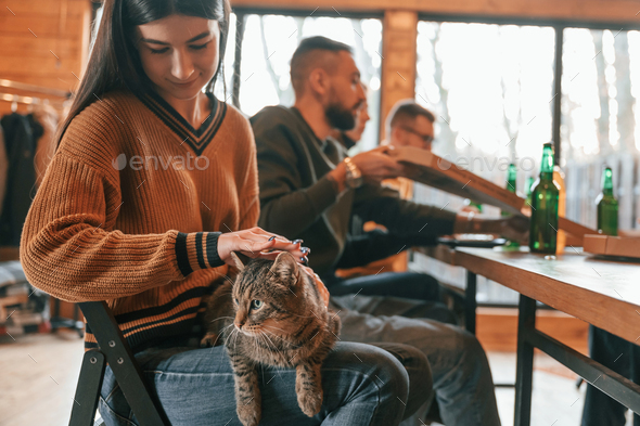 Woman strokes a cat. Group of friends is having good weekend indoors in the wooden building together