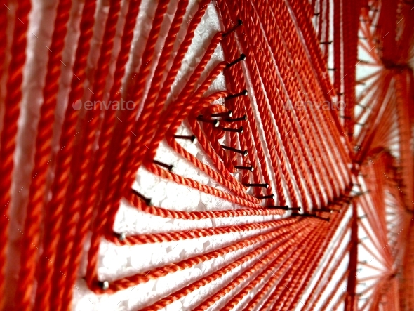 Extreme closeup of homemade abstract art using red string and nails on a white surface
