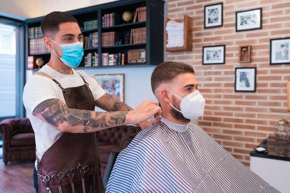 Young hairdresser with tattoos styling the male customer's hair in a  barbershop Stock Photo by wirestock