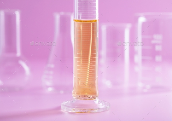Closeup shot of a measuring cylinder flask with yellow liquid on a pink background at a lab