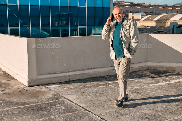 Middle aged bearded man having conversation on mobile phone,while walking near of office building - Stock Photo - Images
