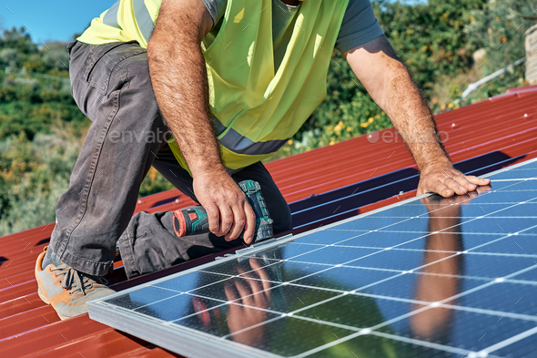 Man's hands with drill installing stand-alone photovoltaic solar panel system on rooftop of a house - Stock Photo - Images