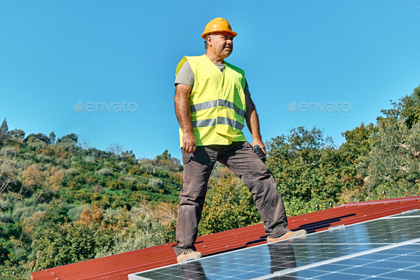 Professional worker with drill installing stand-alone photovoltaic solar panel system on the rooftop