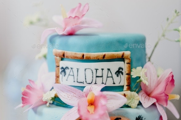 Closeup shot of a Hawaiian thematic cake decorated with pink flowers and \'aloha\' text