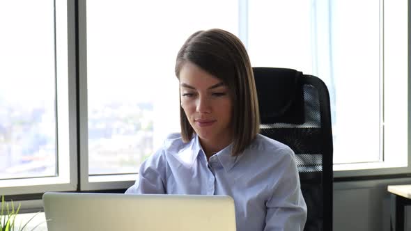 Happy young businesswoman is analizing financial documents on laptop at office alt