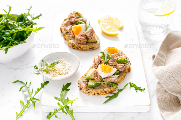 Tuna toast. Open sandwiches with whole grain bread, canned tuna, boiled egg, avocado and arugula - Stock Photo - Images