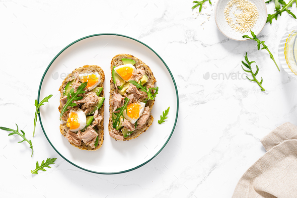 Tuna toast. Open sandwiches with whole grain bread, canned tuna, boiled egg, avocado and arugula - Stock Photo - Images