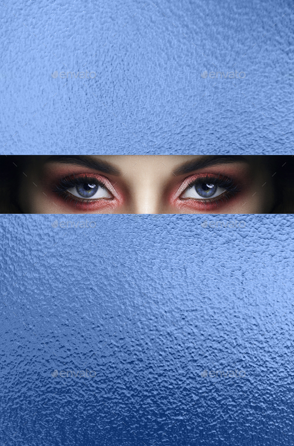 Beauty face pink makeup eyes of young girl in slit hole of blue paper. Woman with beautiful makeup