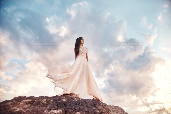 Beautiful woman in a light summer dress beige walks in the mountains. Light dress flutters in wind