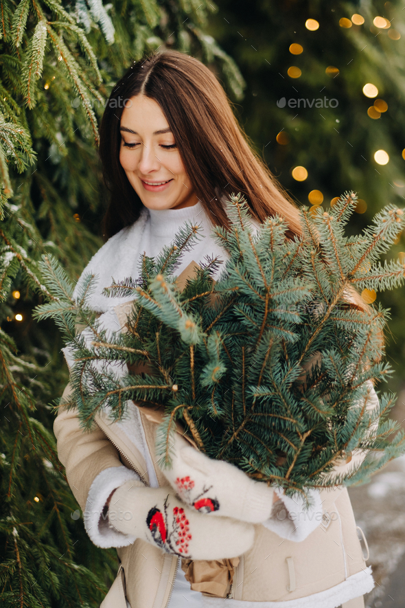 A girl with long hair in winter on the street with a bouquet of fresh fir branches - Stock Photo - Images