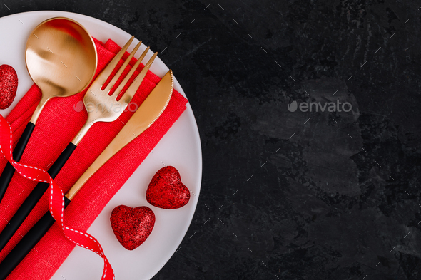 Valentine\'s Day table setting with gold knife, fork, spoon, red ribbon and hearts